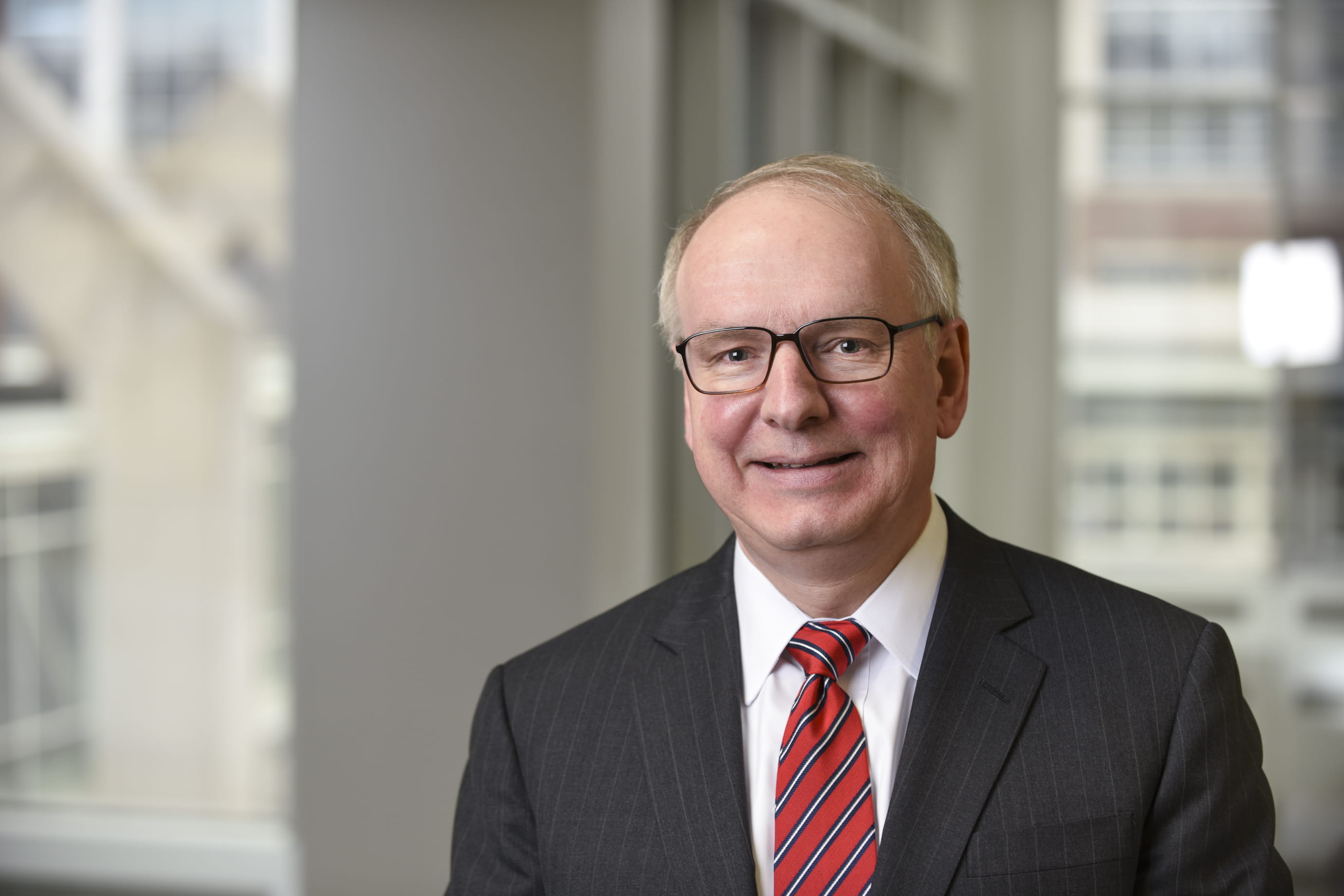 A photo of a smiling man in a suit with a red tie.