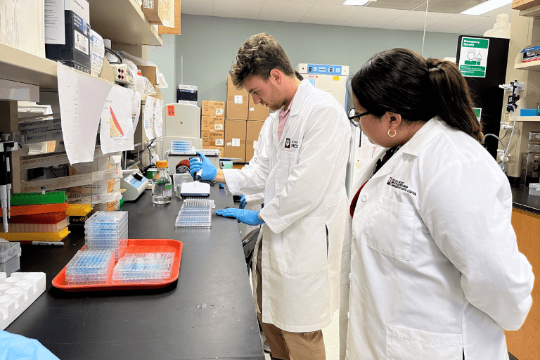 IU School of Medicine intern demonstrating pipetting skill to lab visitor.
