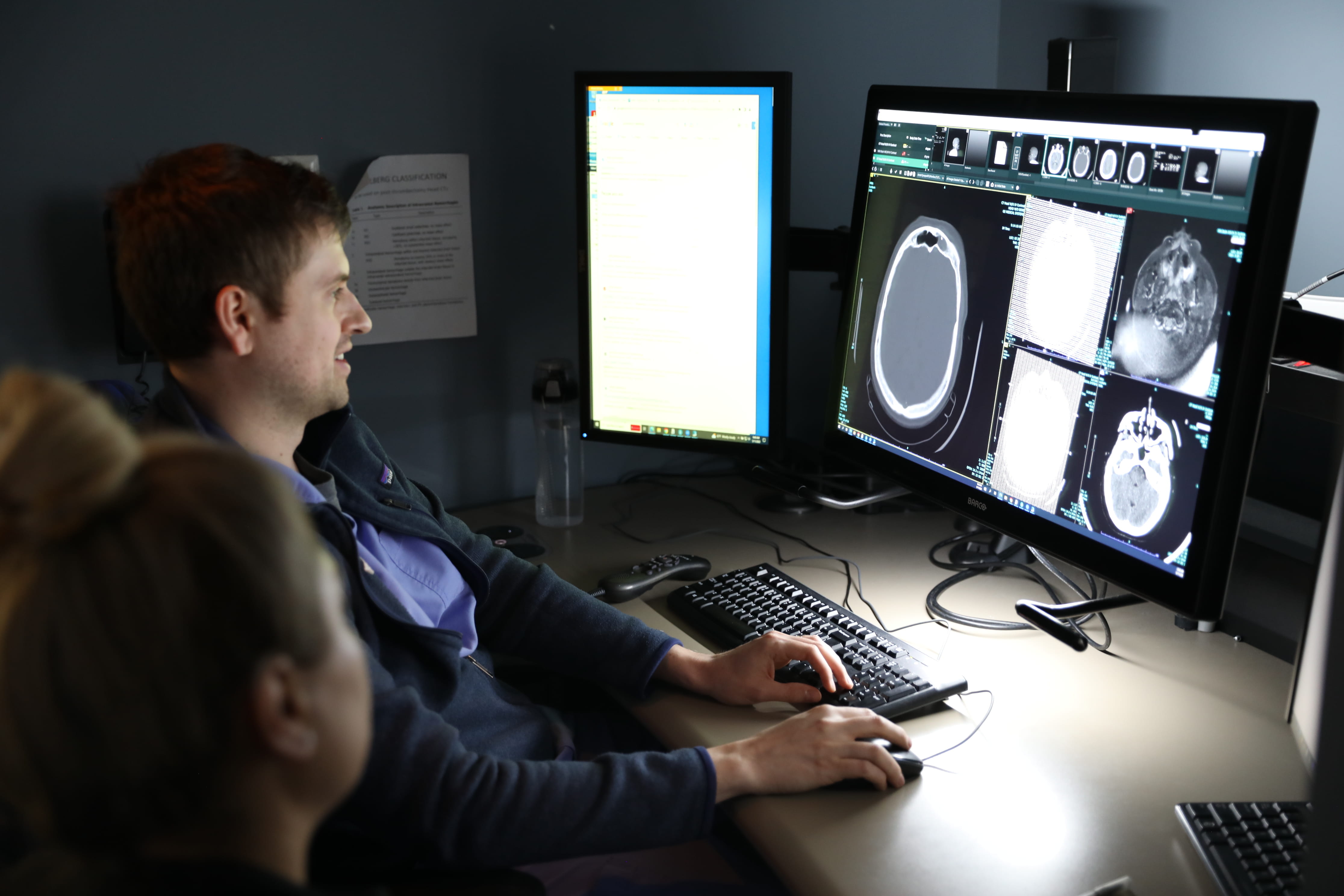 A male radiologist views neuro scans while a female trainee observes.