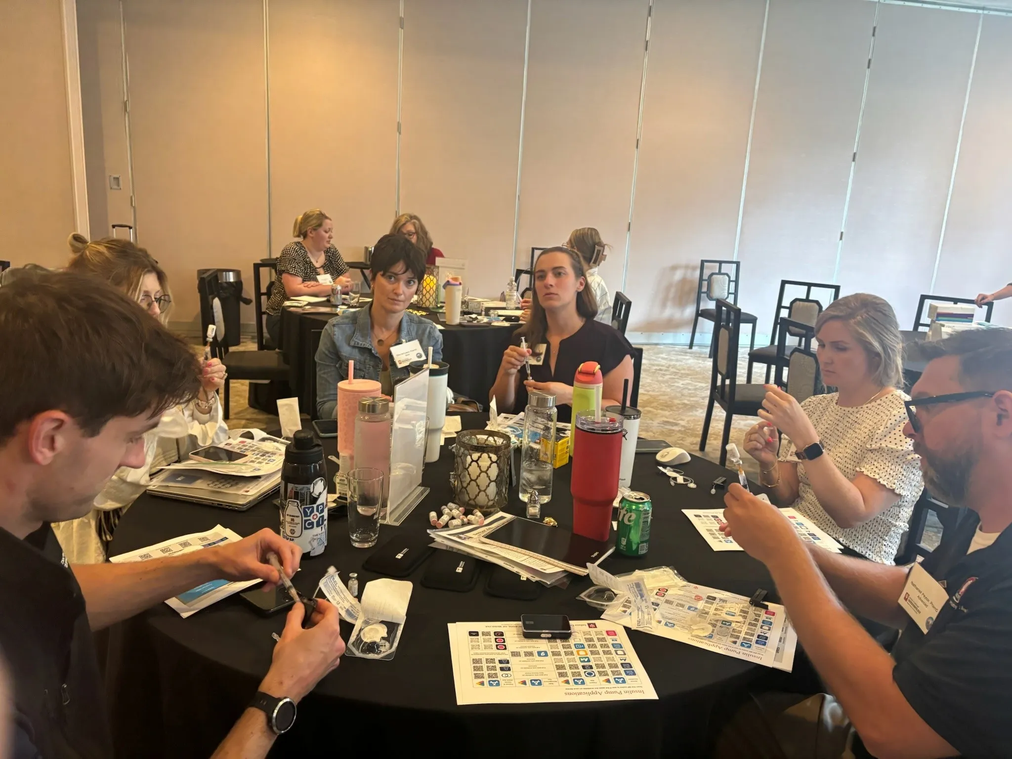 A group of people sit at a round table with hands on diabetes supplies