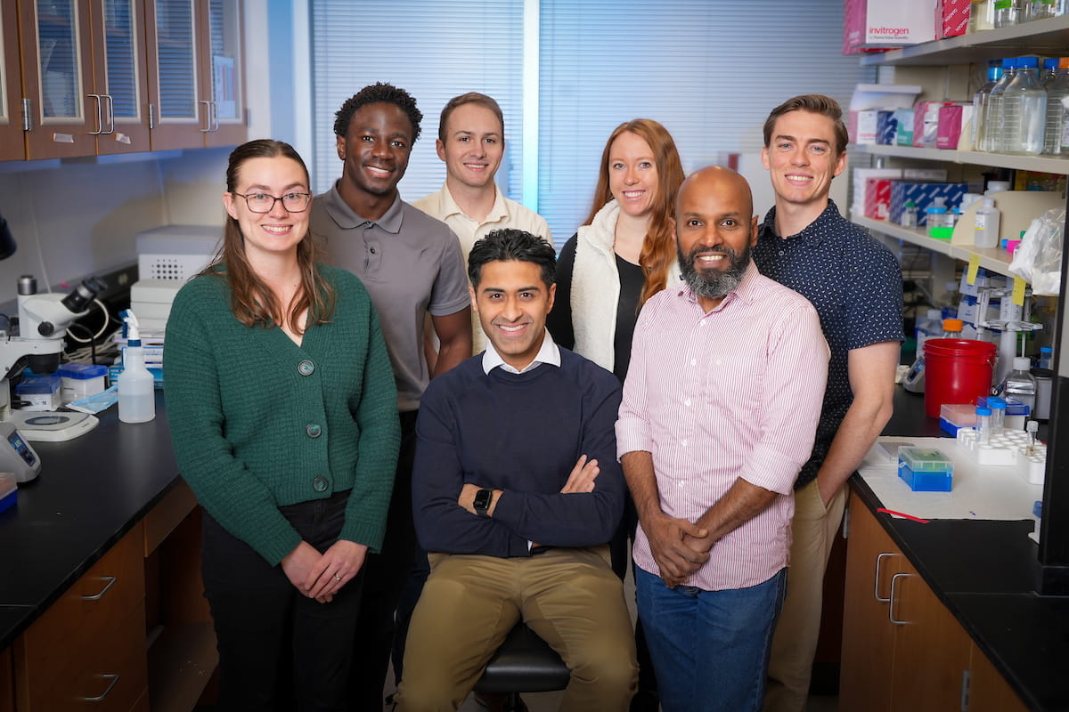 Jignesh Tailor sits on a lab stool surrounded by six members of his research group.