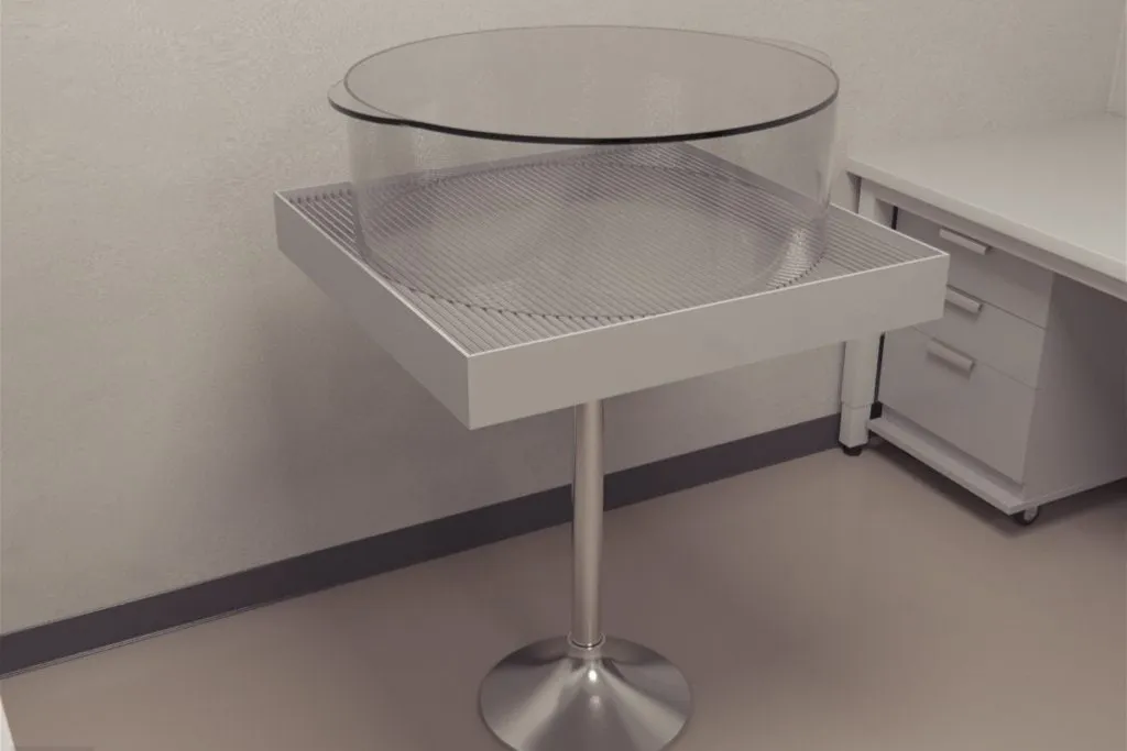 Clear circular instrument sitting on white one legged stand. 