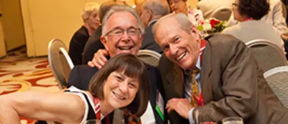 three alumni lean in together and smile at a celebration dinner