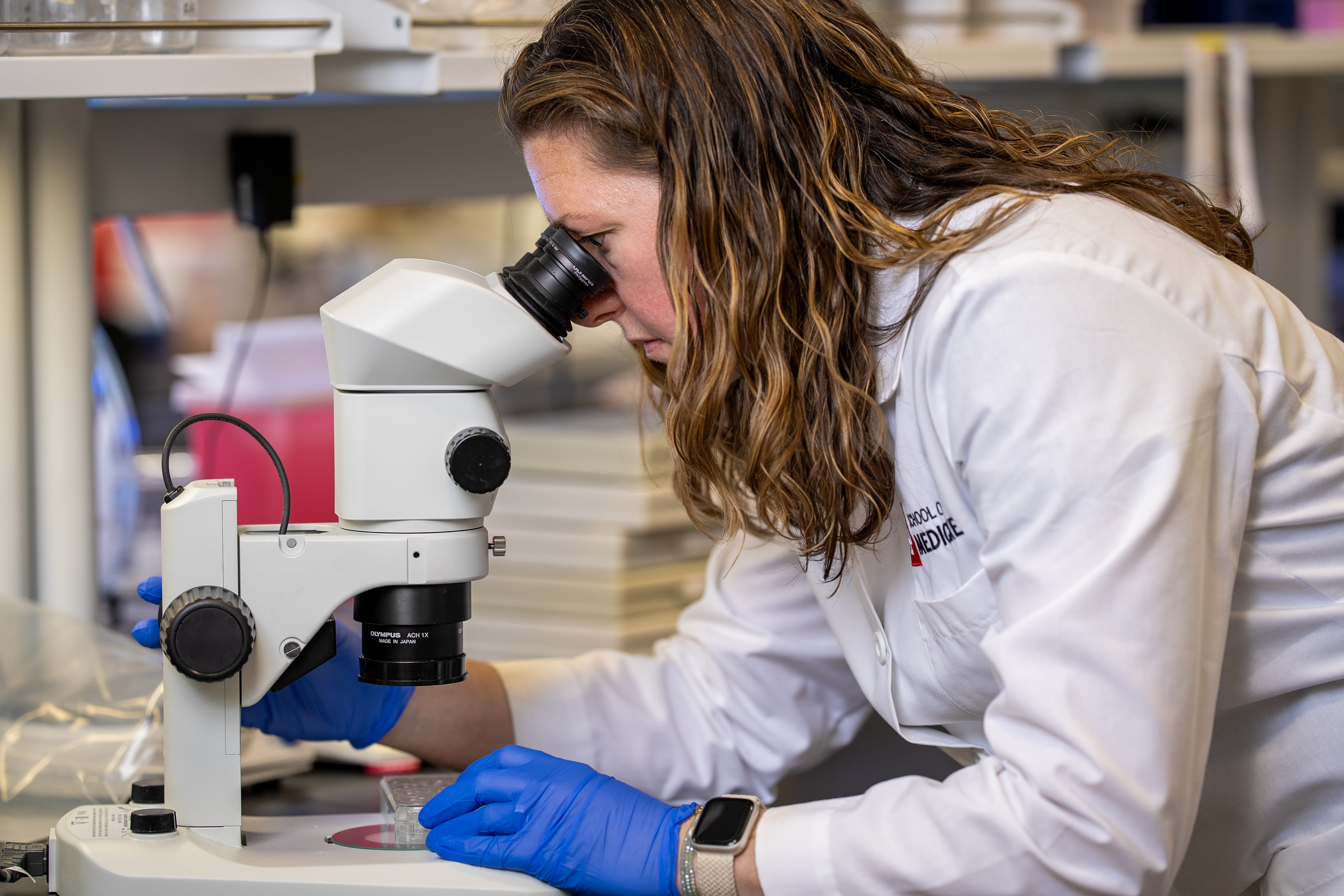 A woman in a lab coat looks into a microscope