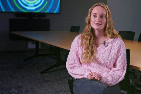 IU medical student Annie Gowan, dressed in a pink sweater, sits before a TV display.