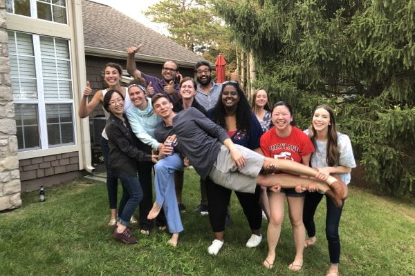 A group of IU Surgery trainees pose for a photo while several members hold another trainee horizontally at shoulder height. 