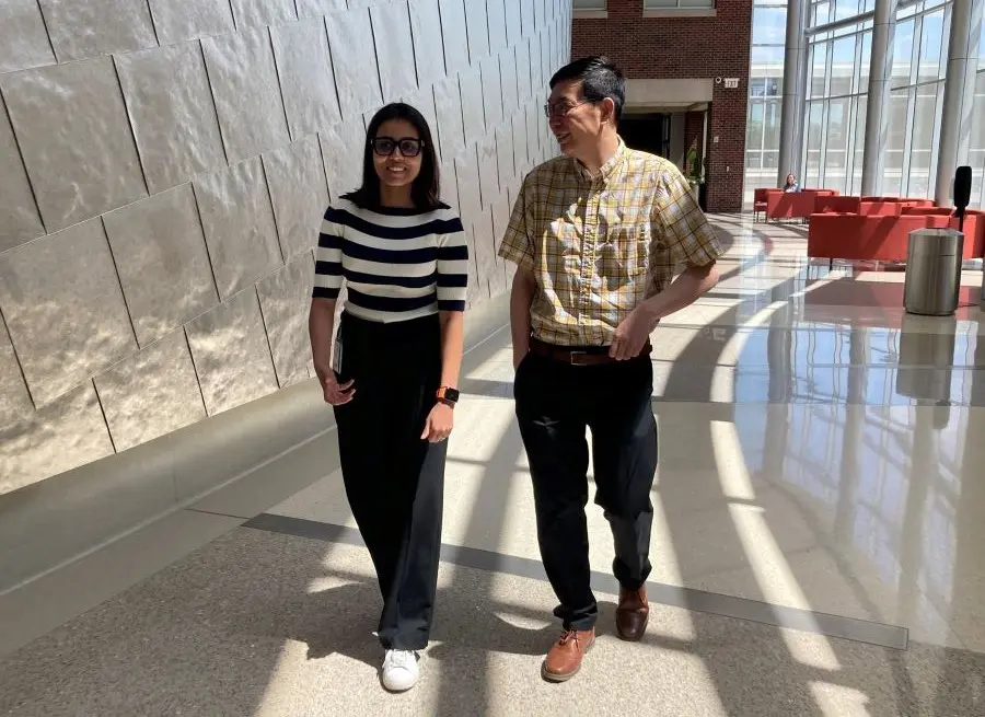 Bhavana Sivakumar walks with her mentor Shing Fai Chan in a hallway with windows and architectural features at the IU School of Medicine.