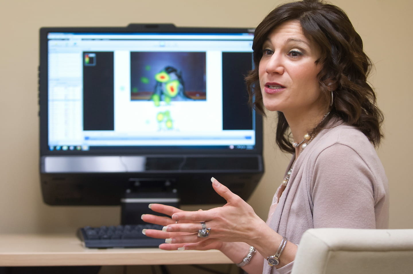 Dawn Neumann gestures with her hands as she speaks about data on a computer monitor in the background