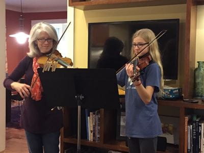 Cavaghan and her daughter stand side by side playing the violin together. Cavaghan and her daughter stand side by side playing the violin together.