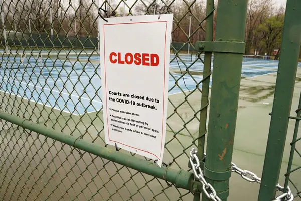 a sign on a fence around a tennis court announcing the court is closed due to COVID
