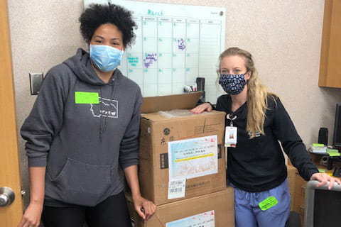 Elizabeth Day and Courtney Raab stack boxes of donated surgical masks