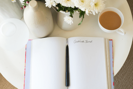 journal that says "Gratitude Journal", cup of coffee and flower vase