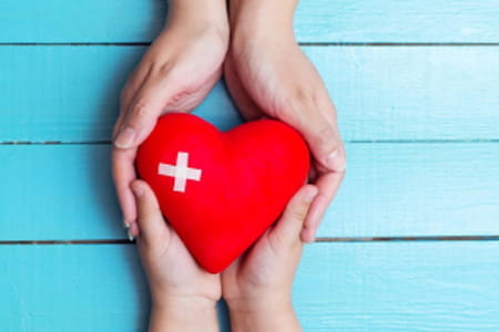 a set of hands holds a heart with a medical plus sign