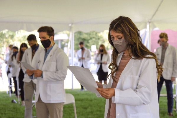 Woman in mask reading physicians oath under tent outside