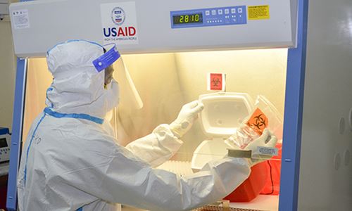 Lab personnel prepare a COVID-19 test in equipment labeled with USAID.