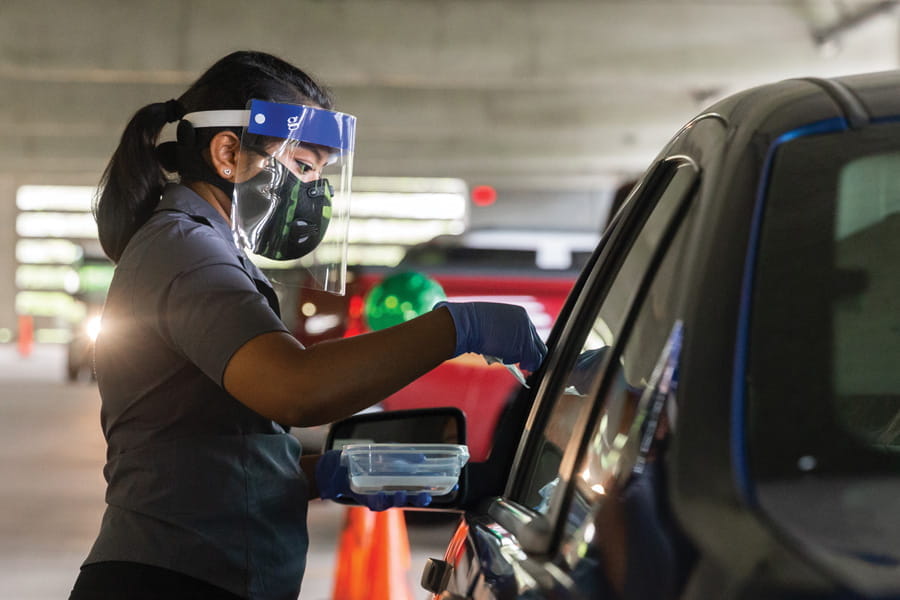 an employee passes out mitigation tests to people in a line of cars