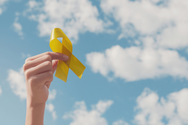Hand holding up yellow ribbon against sky