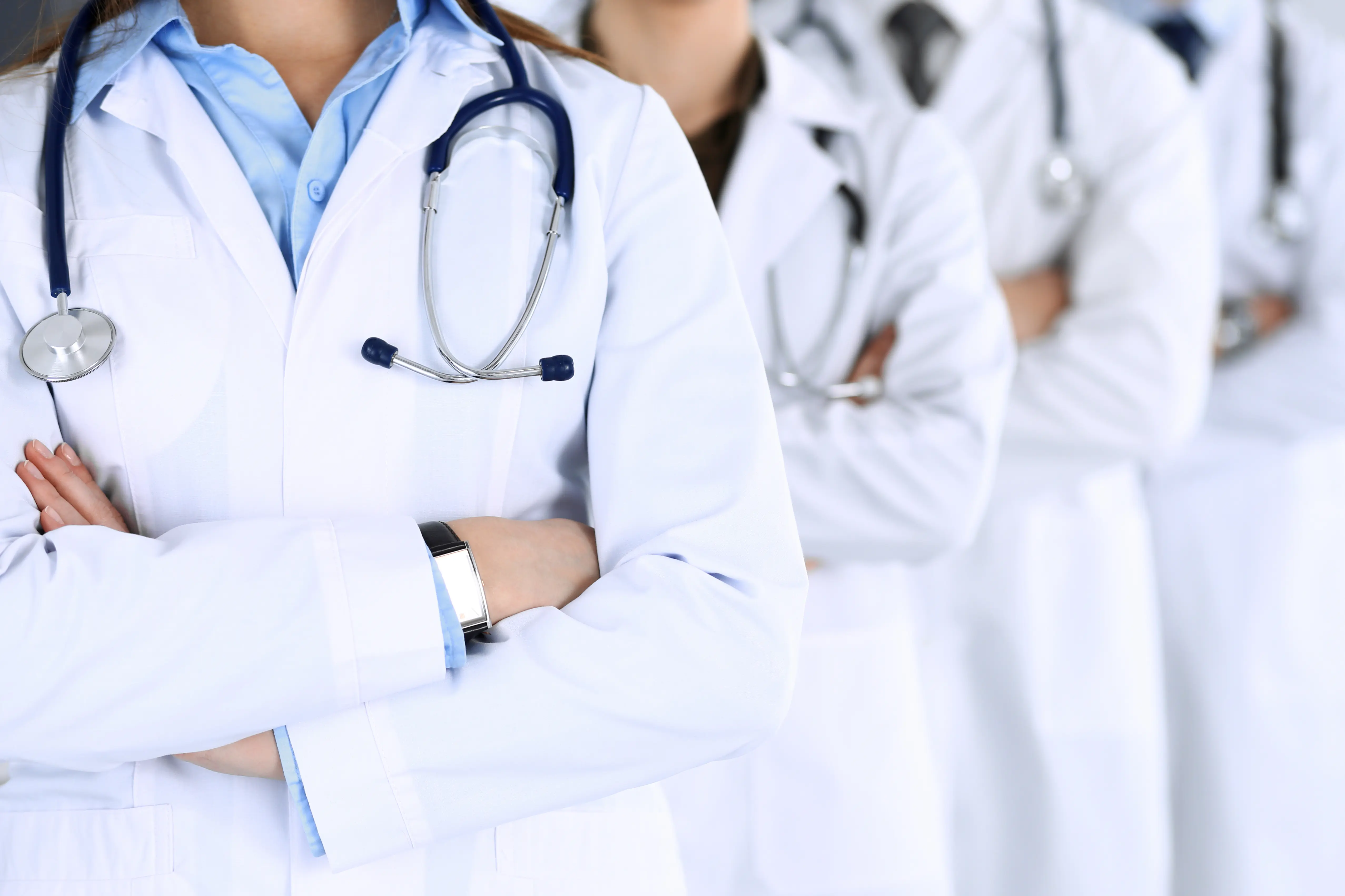 Group of four doctors, from the shoulders down, standing as a team with arms crossed in hospital office.