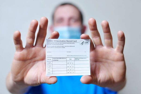 hands holding a COVID vaccination card with blurred face in the background