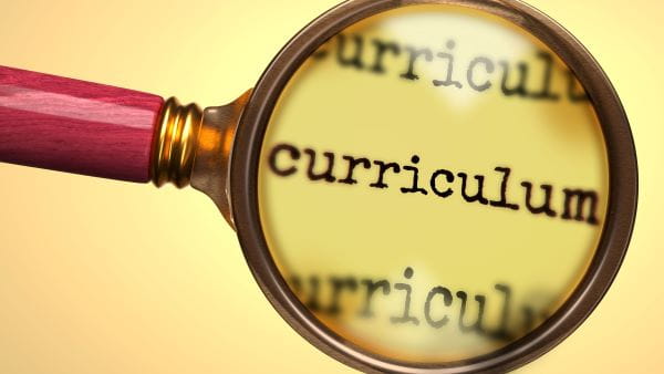 Red handled magnifying glass over the word curriculum with a yellow background 
