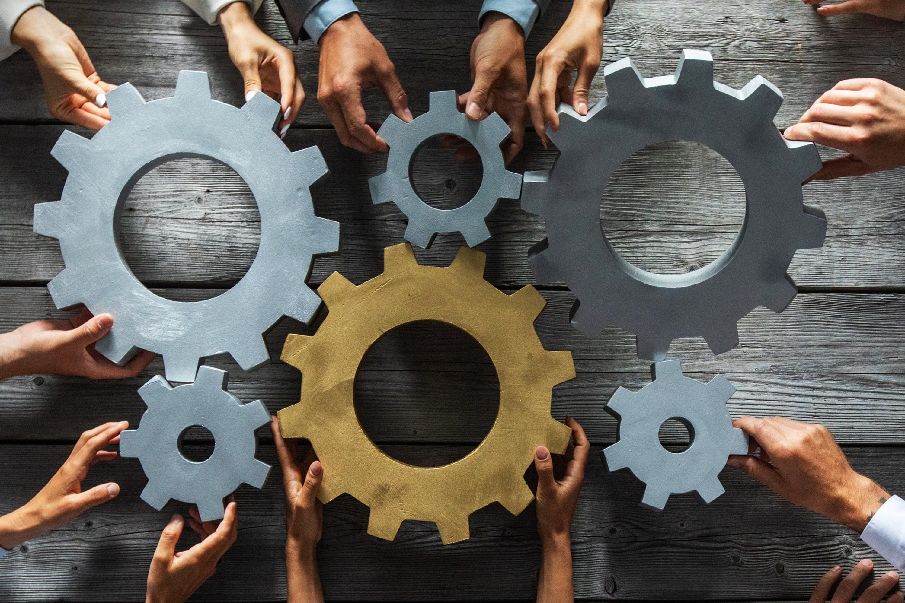 6 gears being joined by people's hands. 