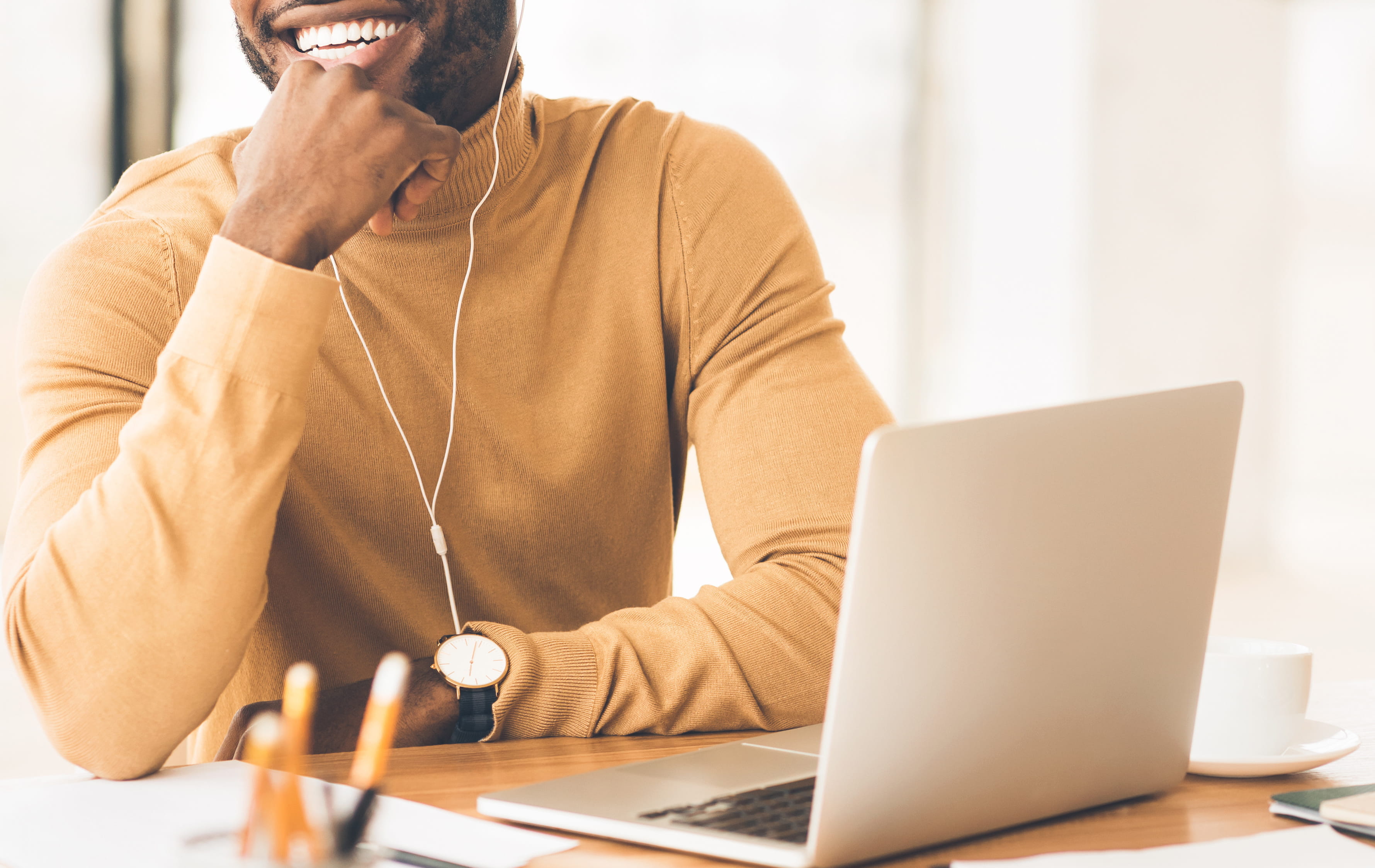 Smiling Black man with a laptop and headphones sitting a desk in a well-lit room