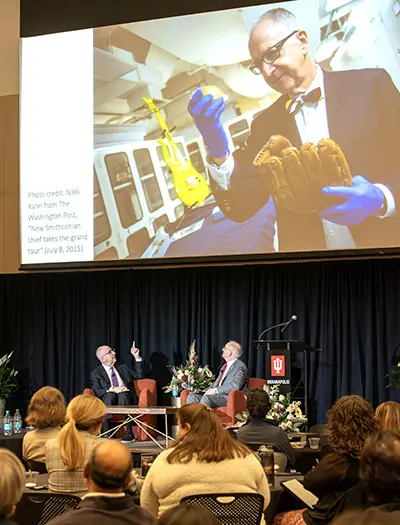 Skorton points to a photo of himself holding a ball signed by one baseball legend (Babe Ruth) and the mitt once used by another (Sandy Koufax) during his time as secretary of the Smithsonian Institution.