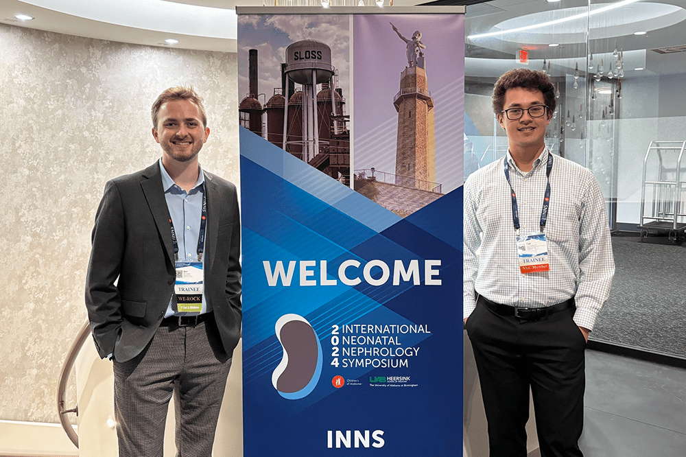 Ben Holland and Carl Russell pose in front of a sign at the International Neonatal Nephrology Symposium.