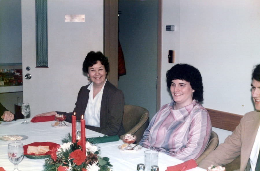Marilyn Baker sits at a table decorated for Christmas in 1985 with colleague MaryAnn Underwood seated to her right.