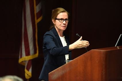 Michelle Howenstine at a podium, wearing a business suit, making a presentation during orientation