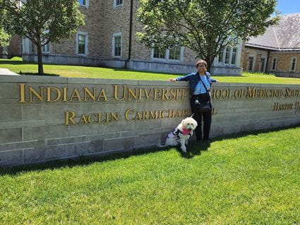 Kennedy Onuoha and service dog Aura outside standing by the IU School of Medicine--South Bend sign.