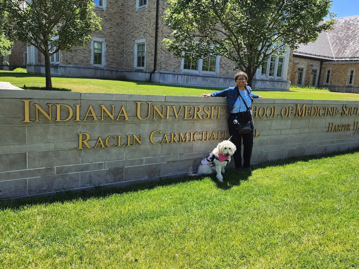 Kennedy Onuoha and service dog Aura outside standing by the IU School of Medicine--South Bend sign.