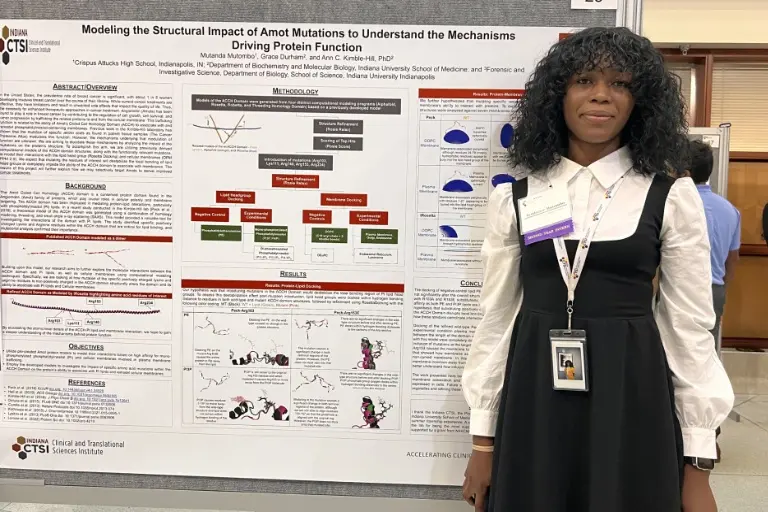 Student, Mutanda Mutombo, standing in front of her research poster at the presentation event.