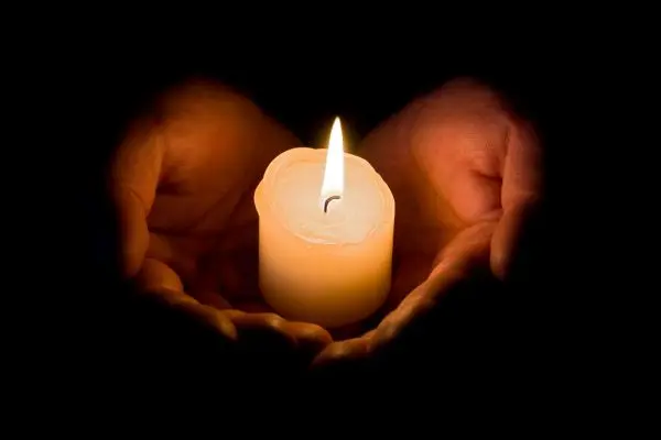 Two hands cradling a lit candle with dark background