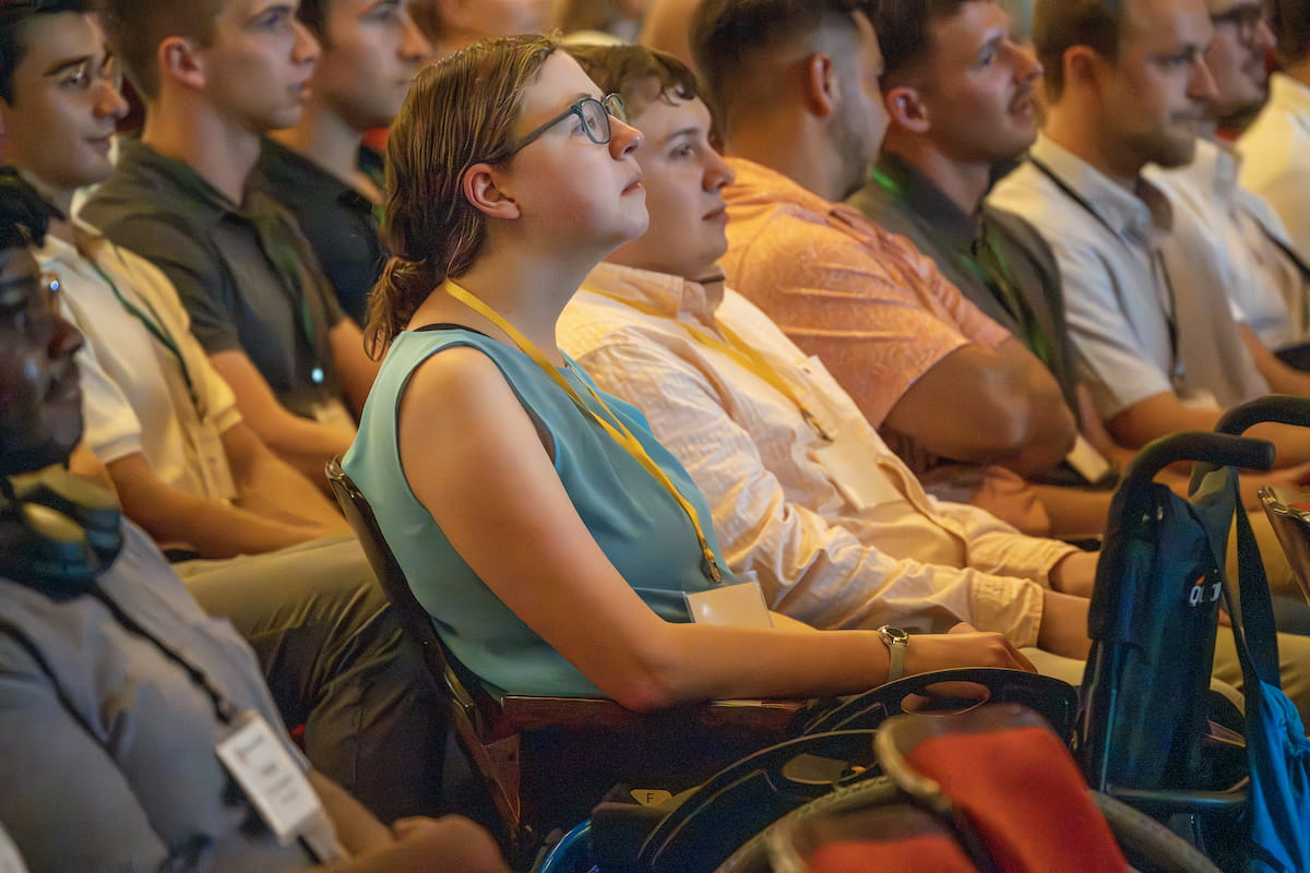 Sarah Vaught, in blue shirt and ID badge, sits among peers in theatre style seating during the opening convocation for IU School of Medicine orientation 2024.