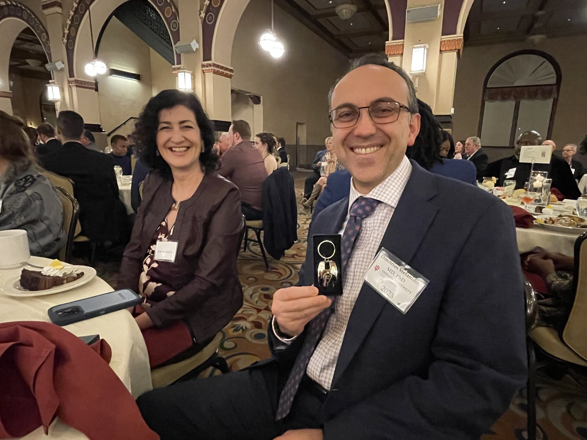 Dr. Dimitrios Stefanidis holding up his AOA induction pin. His wife can be seen sitting behind him.