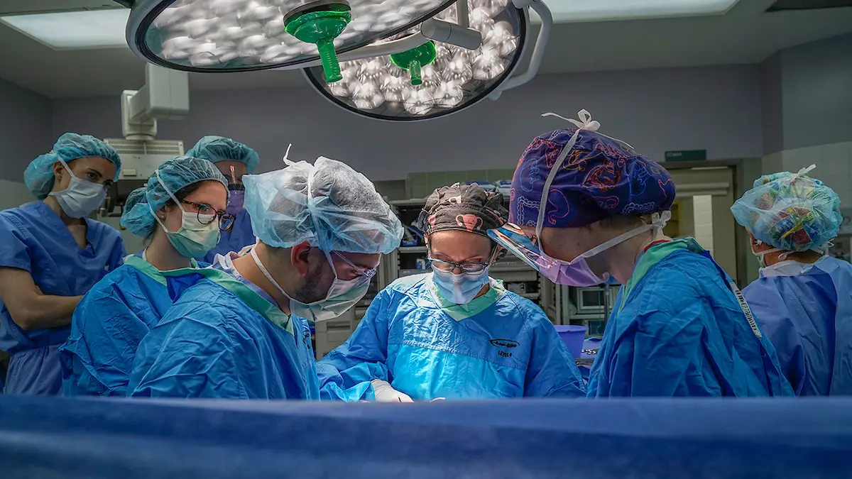 Surgical room with physicians in protective gear; Dr. Kasper leads surgery with trainees assisting