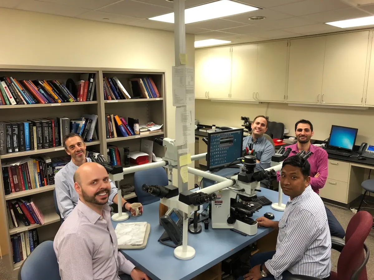 Dr. Krishna sits at a microscope with four other men around the table