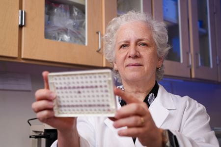 Lilian Plotkin, in white coat, examines a piece of equipment in her laboratory at IU School of Medicine.