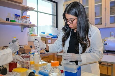 Daya Hernandez wears a white coat and works with a pipette in the Plotkin Lab.