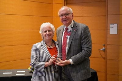 Lilian Plotkin, white woman with white hair and striped blazer, poses with her award and Dean Jay L. Hess