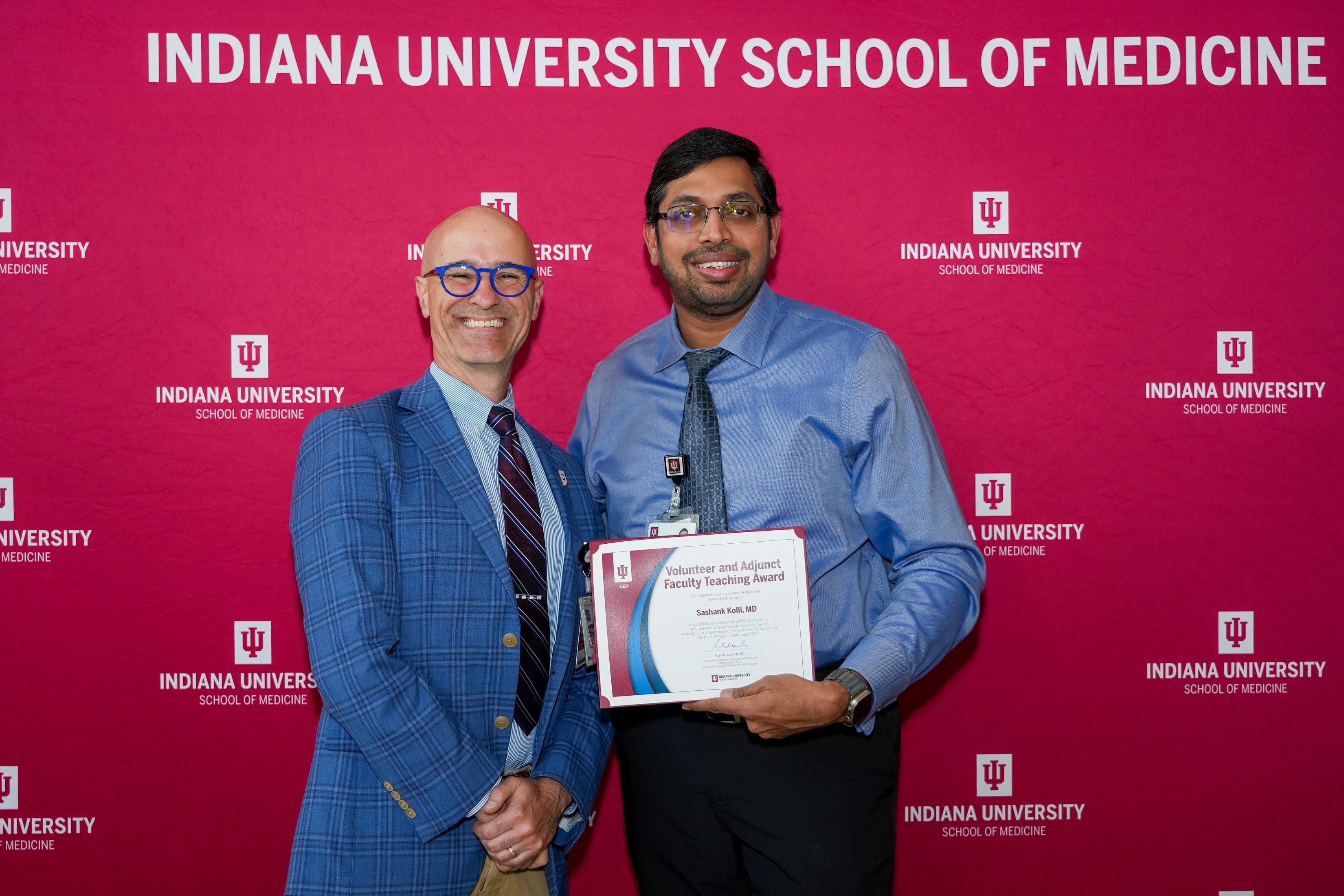 Department of Medicine Chair David Aronoff and Teaching Award winner Sashank Kolli, MD, of IU School of Medicine--Muncie pose with Kolli's award in front of a red, branded IU School of Medicine backdrop