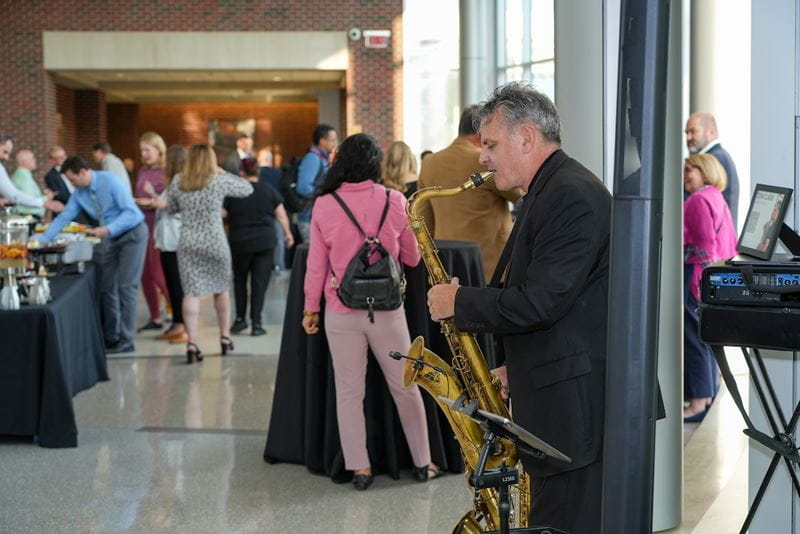 A saxophonist plays in the foreground at the Fall 2024 All-School Meeting reception in the Walther Hall atrium.