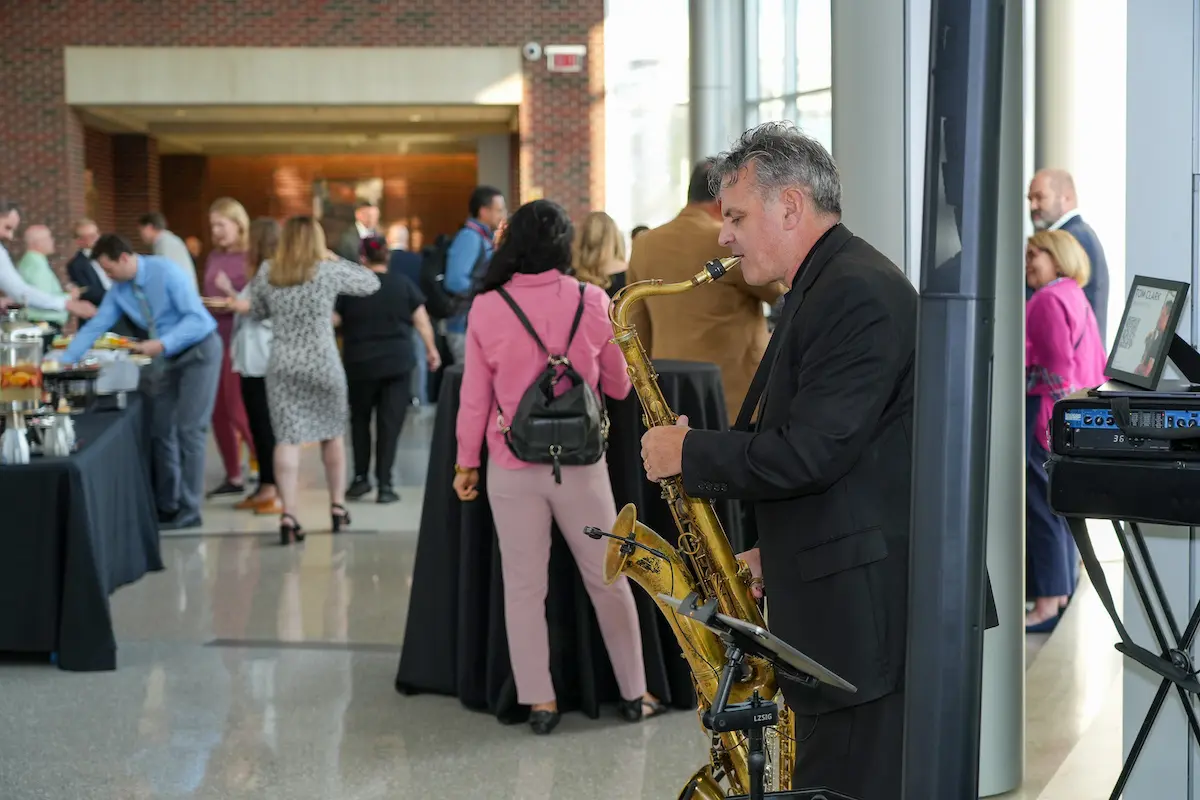A saxophonist plays in the foreground at the Fall 2024 All-School Meeting reception in the Walther Hall atrium.