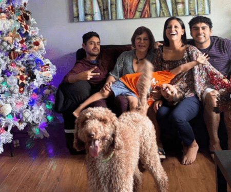 The Castillo family--four adults and one child sits on a couch near Christmas tree with curly-haired dog in foreground