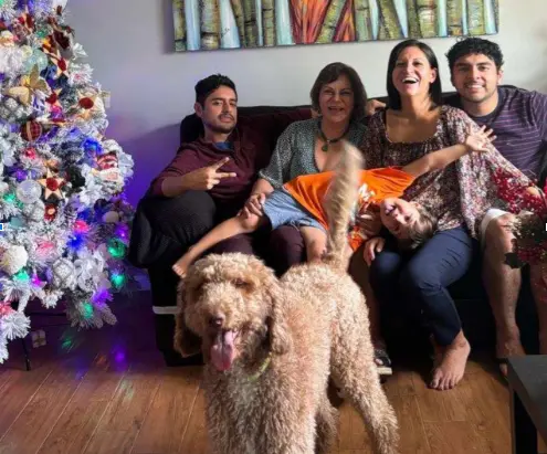 The Castillo family--four adults and one child sits on a couch near Christmas tree with curly-haired dog in foreground