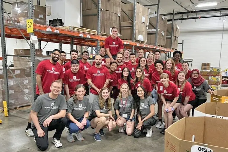 a large group of students in matching red and gray tshirts gather for a photo at the Food Finders Food Bank