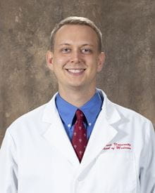 Headshot of David Gunderman in white coat with blue shirt and red tie