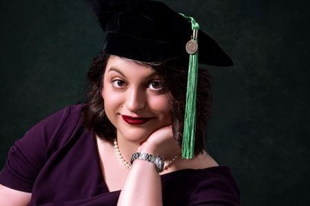 Hannah Kline in her graduation cap with green tassel, black formal background