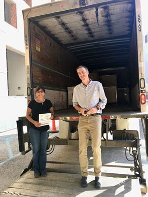 Debra Wood and Dr. Simon Warren stand at the back of a semi trailer with lab equipment supplies.